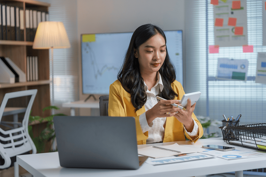 Woman in office using smartphone and laptop.